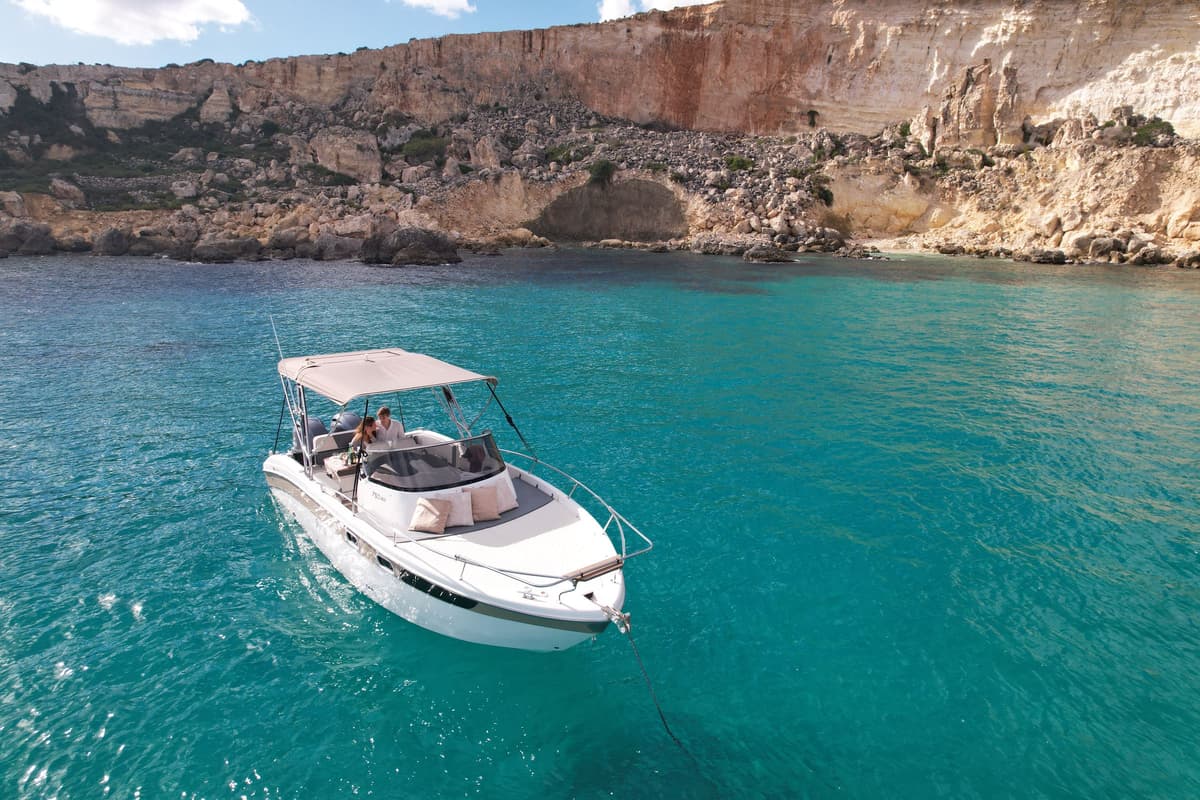 Motor boat anchored in turquoise water below the cliffs of Comino near the Blue Lagoon
